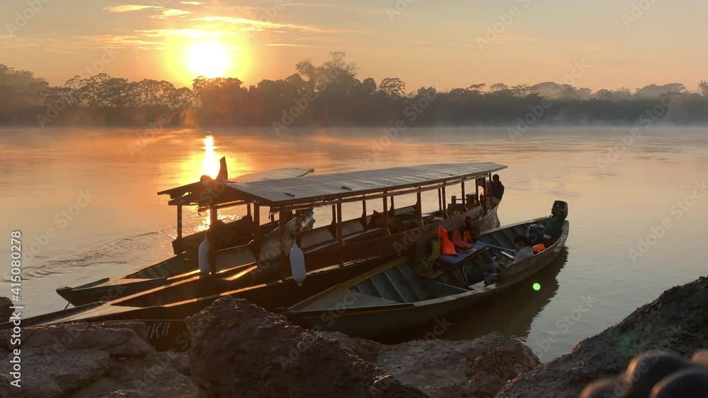 Majestic sunrise at Madre de Dios River with mist rising from water and jungle, local boats anchored in foreground, travel Peru, static shot Majestic sunrise at Madre de Dios River with mist rising from water and jungle, local boats anchored in foreground, travel Peru, static shot