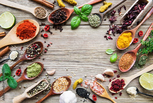 A selection of various colorful spices on a wooden table in  spoons