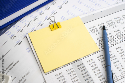 On the financial document is a yellow blank sheet for notes with a blue pen next to a blue notebook. Business and financial concept. Template
