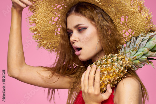 Woman with a gun in hands of a straw hat bright makeup exotic fruits summer pink background