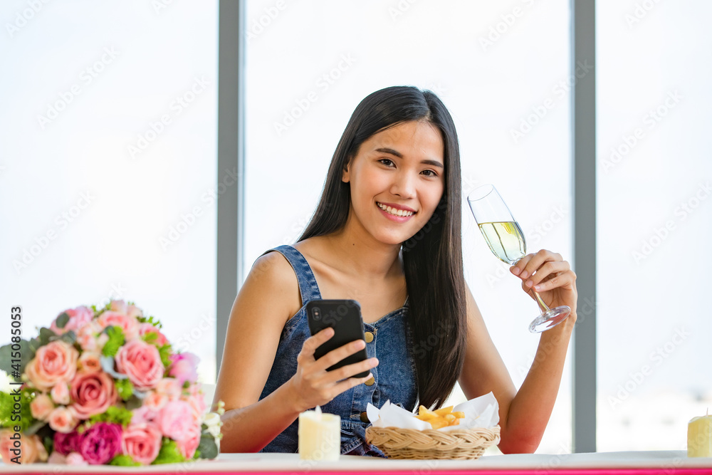 A cute beautiful young Asian woman sitting alone at the fast food shop and holding wine glass and smartphone A cute beautiful young Asian woman sitting alone at the fast food shop and holding wine glass and smartphone
