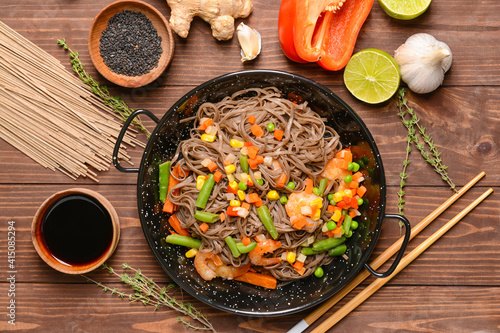 Frying pan with tasty soba noodles and shrimps on wooden background