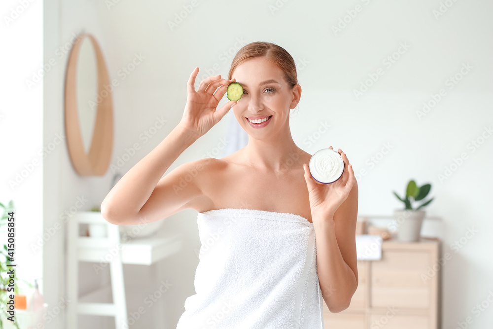 Beautiful young woman with facial cream and cucumber slice in bathroom Beautiful young woman with facial cream and cucumber slice in bathroom