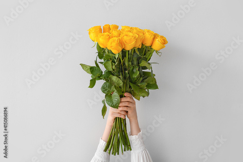 Fototapeta Naklejka Na Ścianę i Meble -  Female hands with beautiful yellow roses on light background