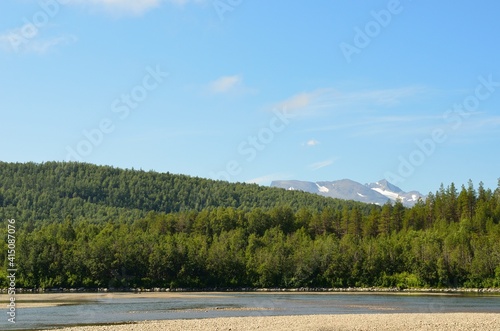 river beach and forest landscape with mountain backdrop in summer sunshine