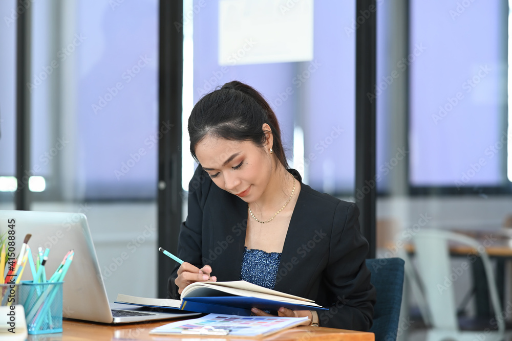 Attractive businesswoman working with computer laptop and writing in an agenda on notebook. Attractive businesswoman working with computer laptop and writing in an agenda on notebook.