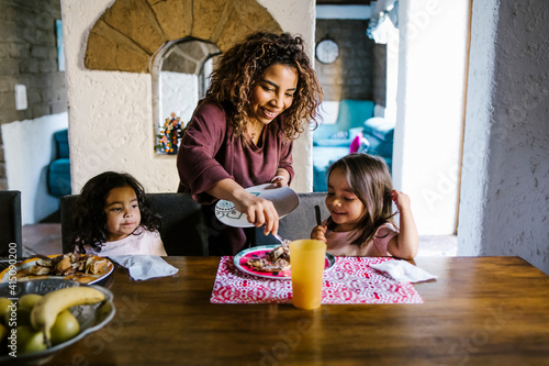 Hispanic mother serving breakfast to her daughters at home in Latin America