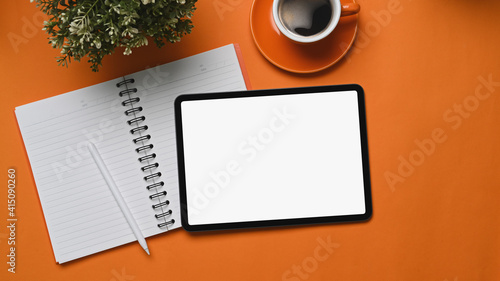 Mock up digital tablet with empty screen  notebook  coffee cup and plant on orange background.