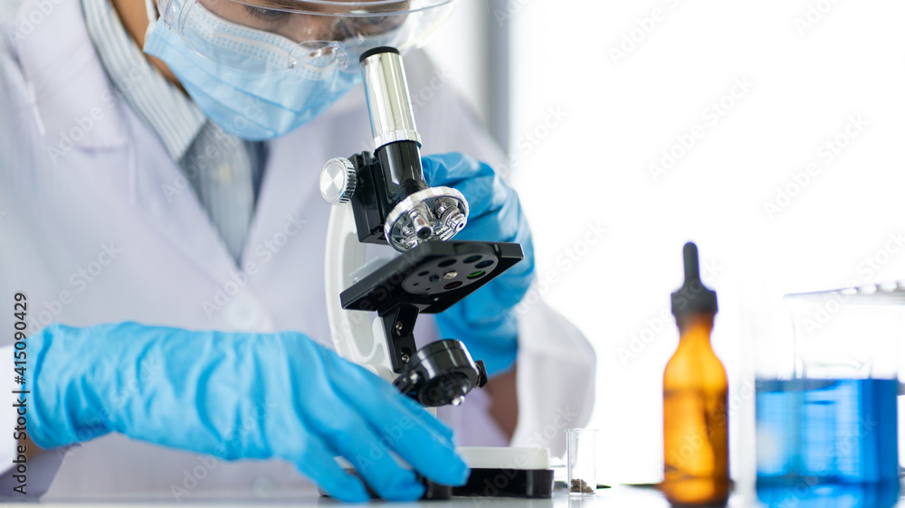 Fototapeta premium Young Asian scientist Working looking through a microscope doing research for analyzing a Experiments sample in a forensic laboratory.
