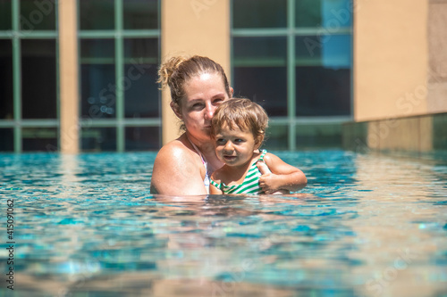 young mother swimng with her little daughter in the pool on the roof of a skyscraper in a metropolis...