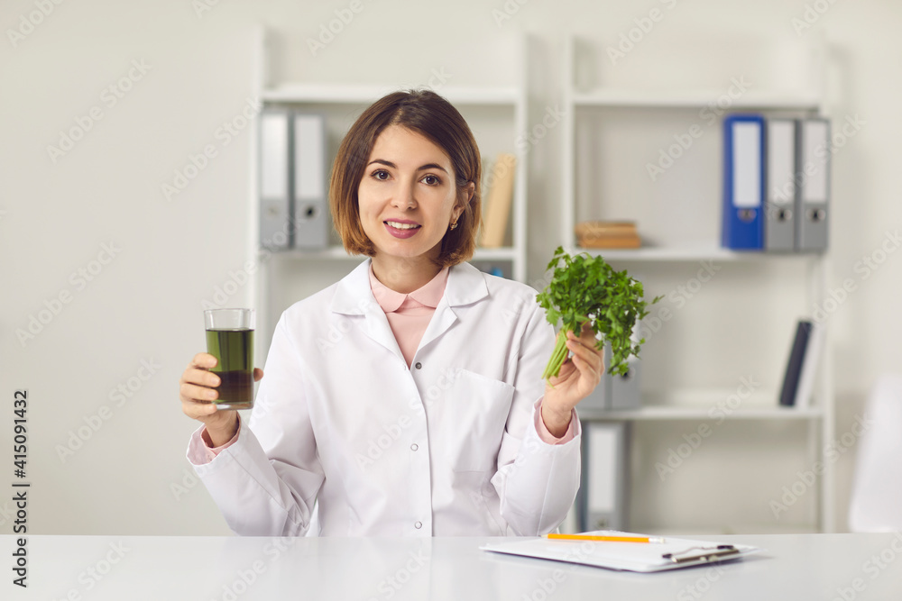 Healthy diet expert recommends fitness beverage. Dietitian or nutritionist looking at camera and holding fresh weight loss detox parsley, coriander or cilantro drink. Webcam portrait in clinic office Healthy diet expert recommends fitness beverage. Dietitian or nutritionist looking at camera and holding fresh weight loss detox parsley, coriander or cilantro drink. Webcam portrait in clinic office