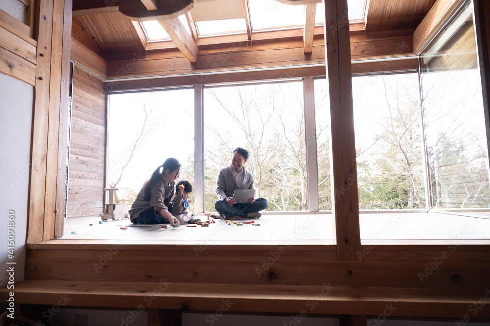 木造のきれいな新築の広い部屋で美人なママと家族団らんの幸せな若いファミリー 下にコピースペースあり 木造のきれいな新築の広い部屋で美人なママと家族団らんの幸せな若いファミリー 下にコピースペースあり