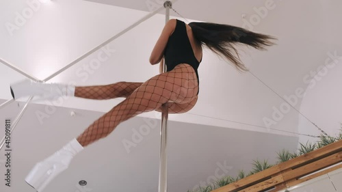 Beautiful athletic woman dancing on the pole. Pole dancer doing an acrobatic stunt.