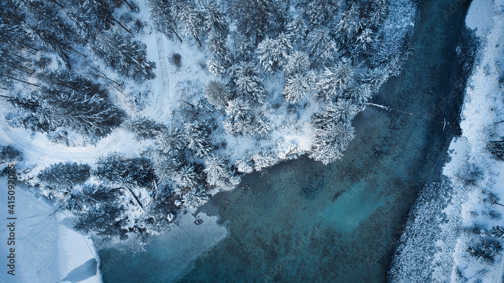 Birds eye view from a drone on a partial frozen lake in a winter landscape with trees and a road