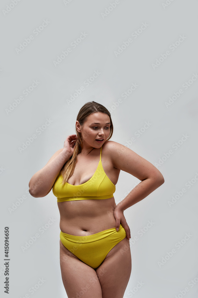 Curious curvy young female model wearing yellow underwear looking away  while posing isolated over light background Stock Photo