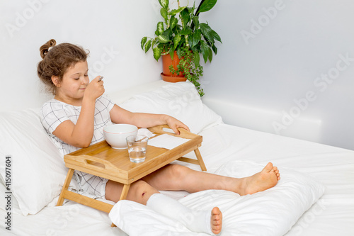 A teenage girl eats in bed on a wooden tray after applying plaster on her leg. Bed rest and care for the patient, the child photo