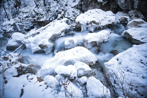 snow covered rocks in a river captured as smooth long exposure; winter landscape