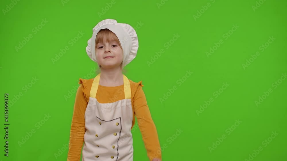 Child girl dressed in apron and hat like chef cook pointing at right on blank space. Place for your advertisement logo. Chroma key background. Nutrition, family cooking school, children education Child girl dressed in apron and hat like chef cook pointing at right on blank space. Place for your advertisement logo. Chroma key background. Nutrition, family cooking school, children education
