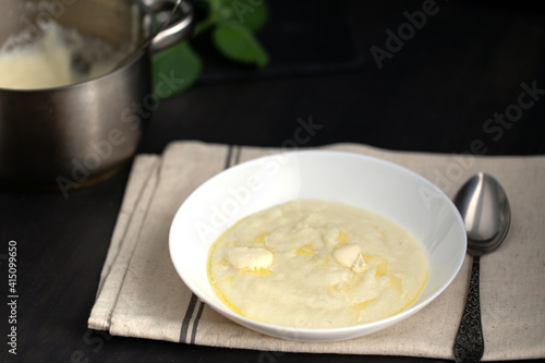 Semolina porridge in white bowl for breakfast on dark wooden table.