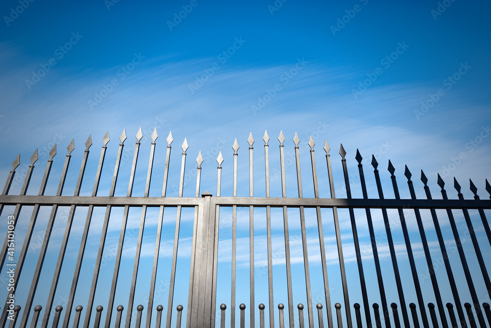 Closeup of a wrought iron gate with sharp points on blue sky with clouds and copy space. Closeup of a wrought iron gate with sharp points on blue sky with clouds and copy space.