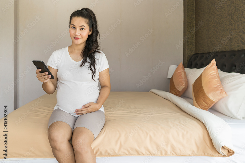 Pregnant mother uses the phone to relax on the bed and look at camera. Pregnant mother uses the phone to relax on the bed and look at camera.