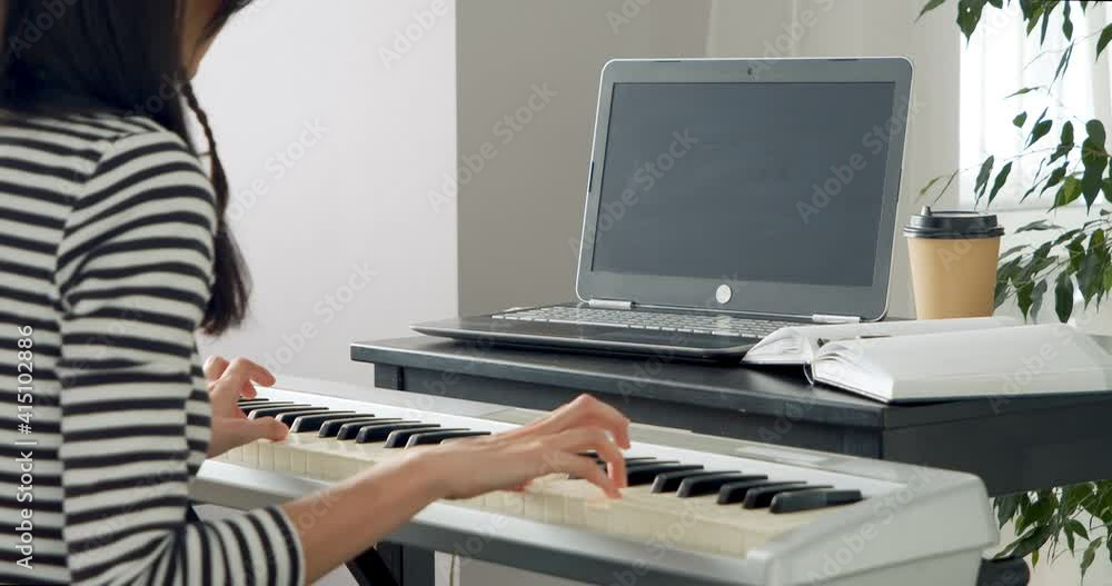 Close-up shot of unrecognizable woman playing electronic piano while learning music online using laptop at home Close-up shot of unrecognizable woman playing electronic piano while learning music online using laptop at home