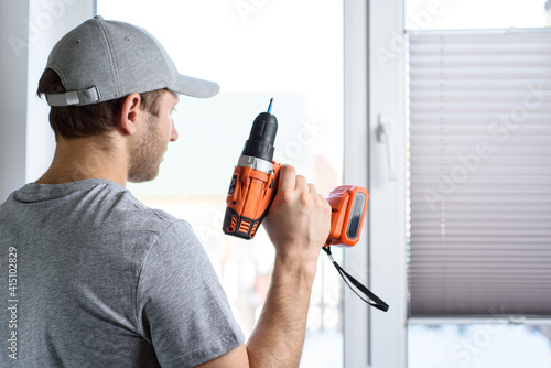 Fotografía Man installing gray pleated blinds on the window with screwdriver