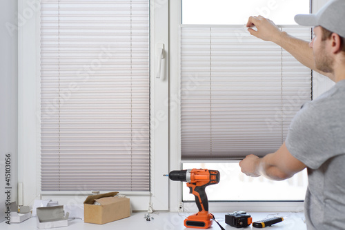 Man installing gray pleated blinds on the window with screwdriver photo
