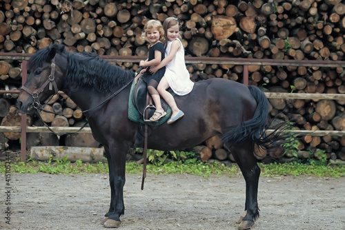 Little girls ride on horse on summer day. Equine therapy, recreation concept. Children smile in rider saddle on horse back.