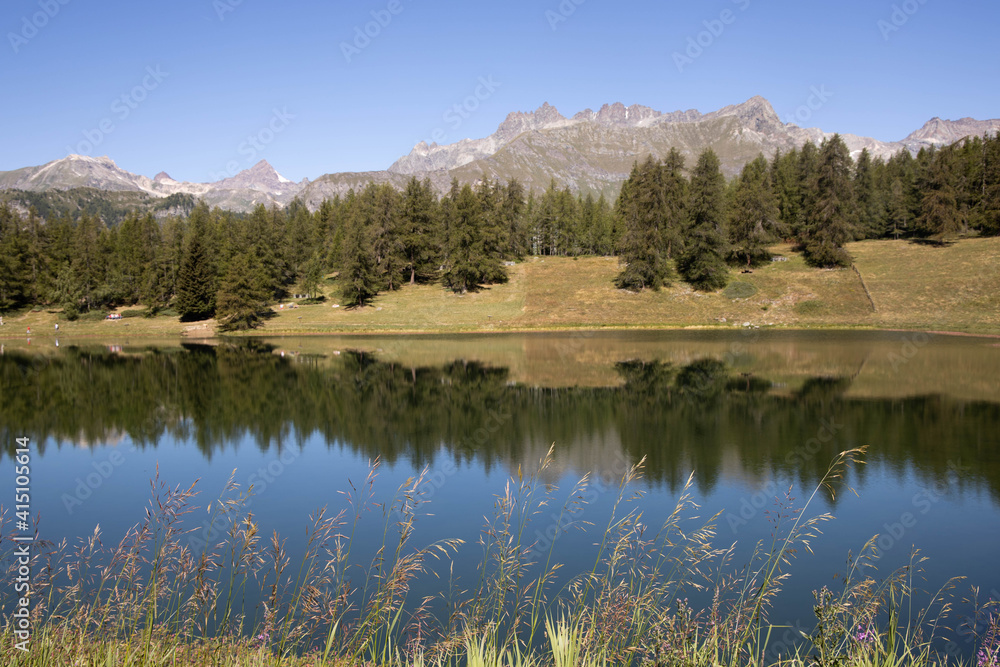 A beautiful large lake with a reflection of the sky, a dense green forest and tall grass. The highest peak of the mountain.