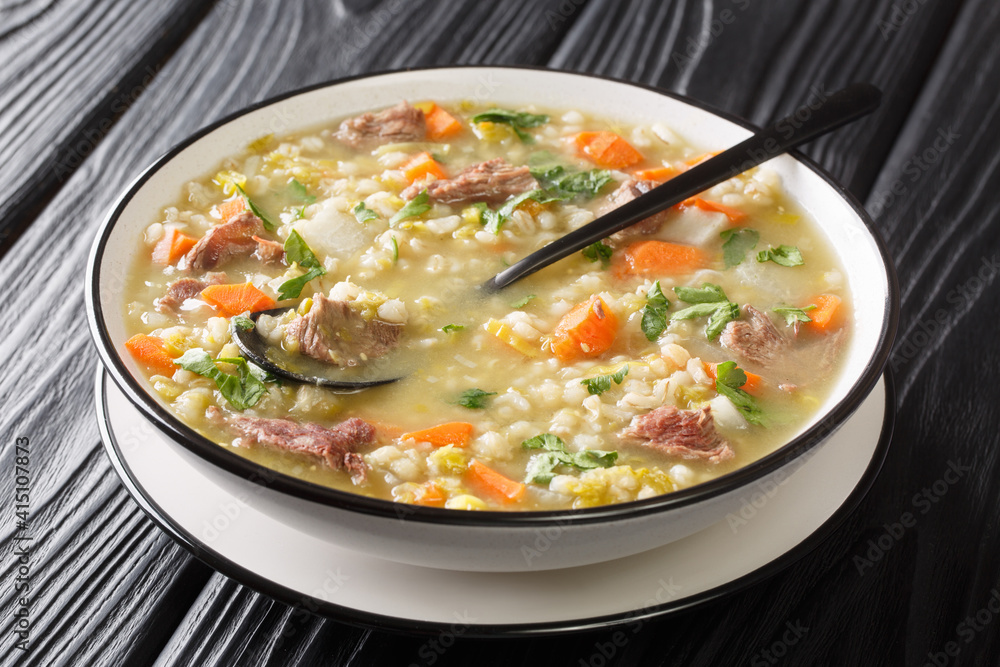 Scotch broth is a Scottish soup traditionally featuring barley, a meat lamb, root vegetables  closeup in the plate on the table. Horizontal
