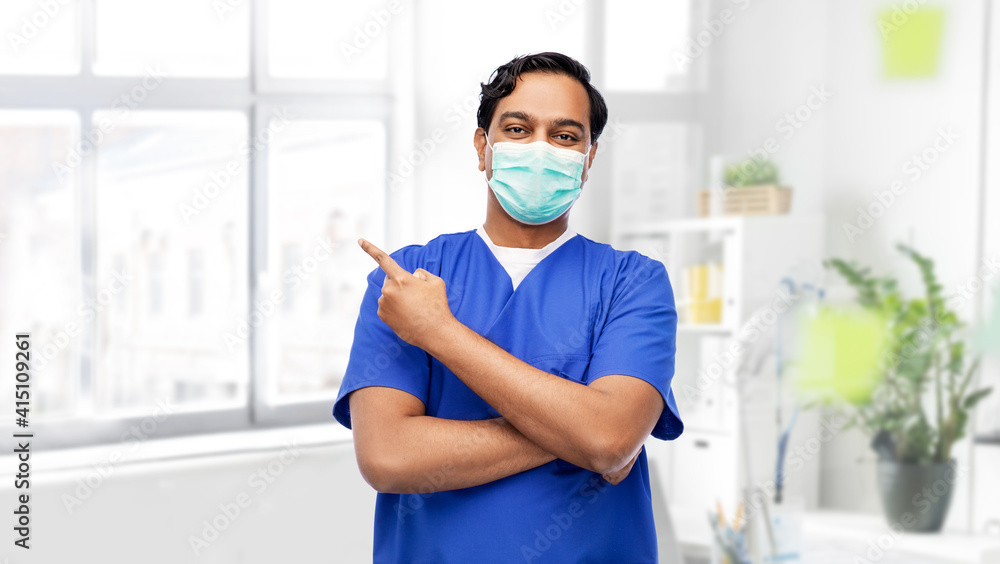 healthcare, profession and medicine concept - indian doctor or male nurse in blue uniform and face protective medical mask showing something imaginary over medical office at hospital on background healthcare, profession and medicine concept - indian doctor or male nurse in blue uniform and face protective medical mask showing something imaginary over medical office at hospital on background
