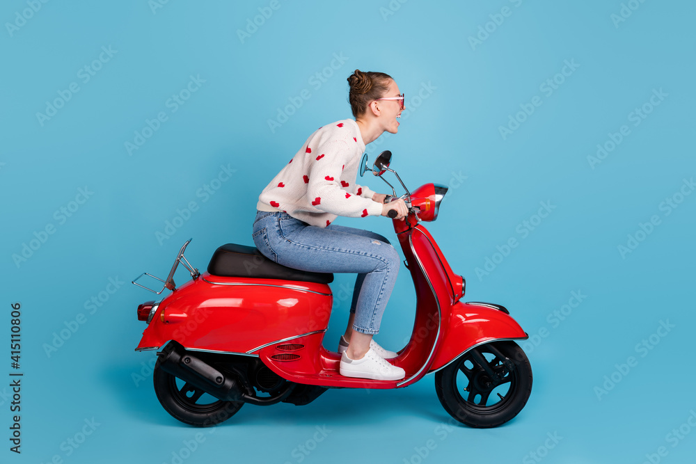 Full size profile side photo of charming excited young woman ride motorcycle on road isolated on blue color background Full size profile side photo of charming excited young woman ride motorcycle on road isolated on blue color background