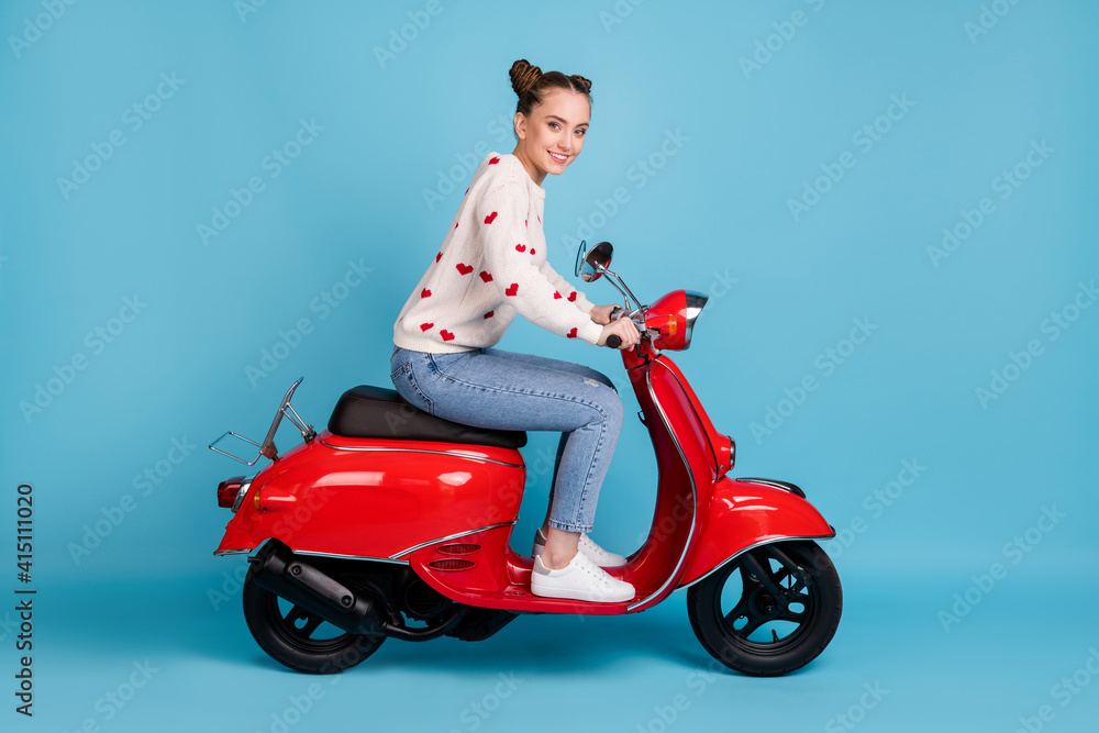 Full length photo of young girl drive scooter wear heart print sweater jeans sneakers isolated blue color background Full length photo of young girl drive scooter wear heart print sweater jeans sneakers isolated blue color background