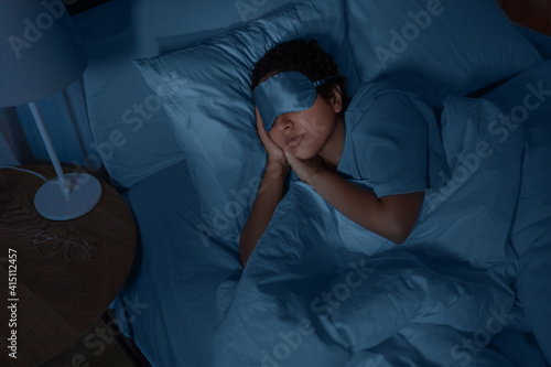 people, relax and comfort concept - young african american woman in eye mask sleeping in bed at home at night photo