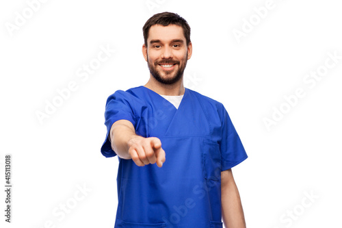 healthcare, profession and medicine concept - happy smiling doctor or male nurse in blue uniform pointing finger to camera over white background © Syda Productions