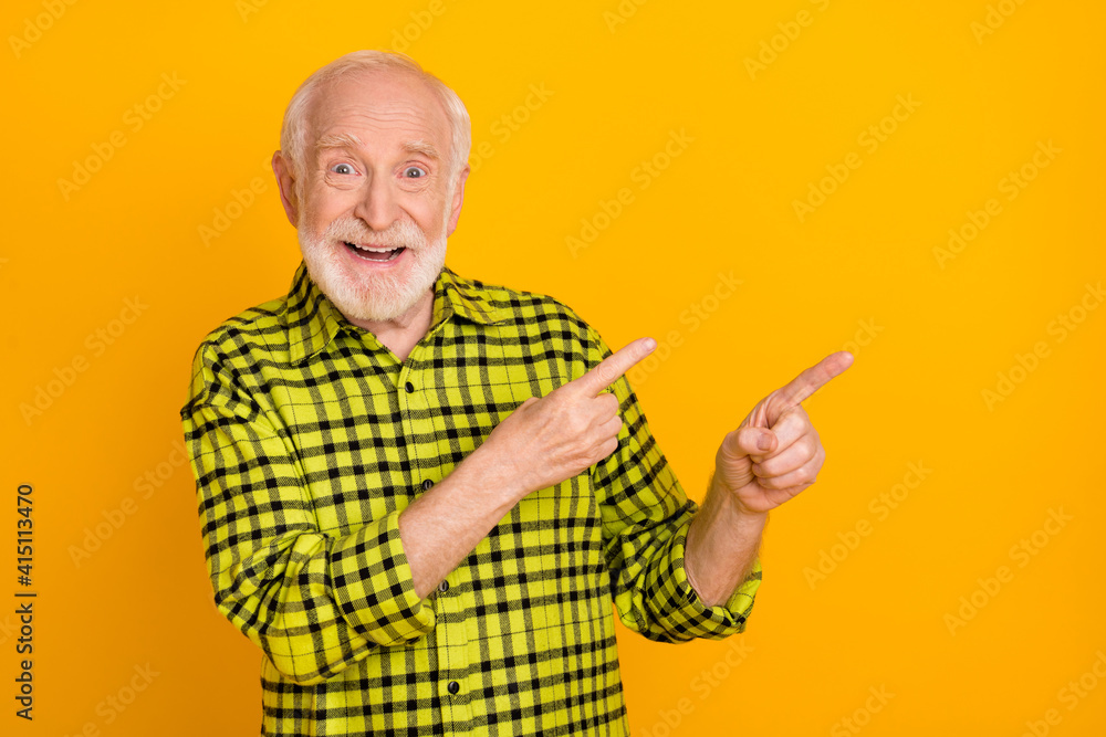 Photo of elderly man happy positive smile indicate fingers empty space ad promo choice decision isolated over yellow color background Photo of elderly man happy positive smile indicate fingers empty space ad promo choice decision isolated over yellow color background