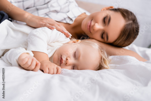 surface level of happy woman with closed eyes touching sleeping son, blurred background