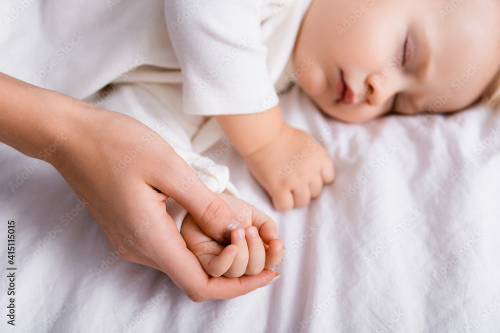 mother touching hand of baby boy sleeping at home, blurred background mother touching hand of baby boy sleeping at home, blurred background