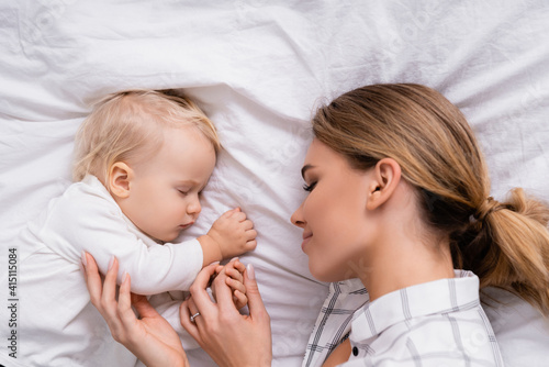 top view of happy woman touching hand of little son sleeping on white bedding