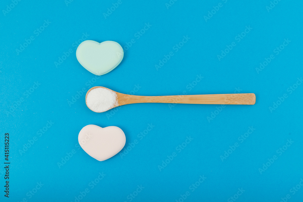 White powder in wooden spoon on blue background with hearts. Top view, copy space White powder in wooden spoon on blue background with hearts. Top view, copy space