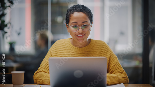 Portrait of Young Latin Marketing Specialist in Glasses Working on Laptop Computer in Busy Creative Office Environment. Beautiful Diverse Multiethnic Female Project Manager is Browsing Internet. photo