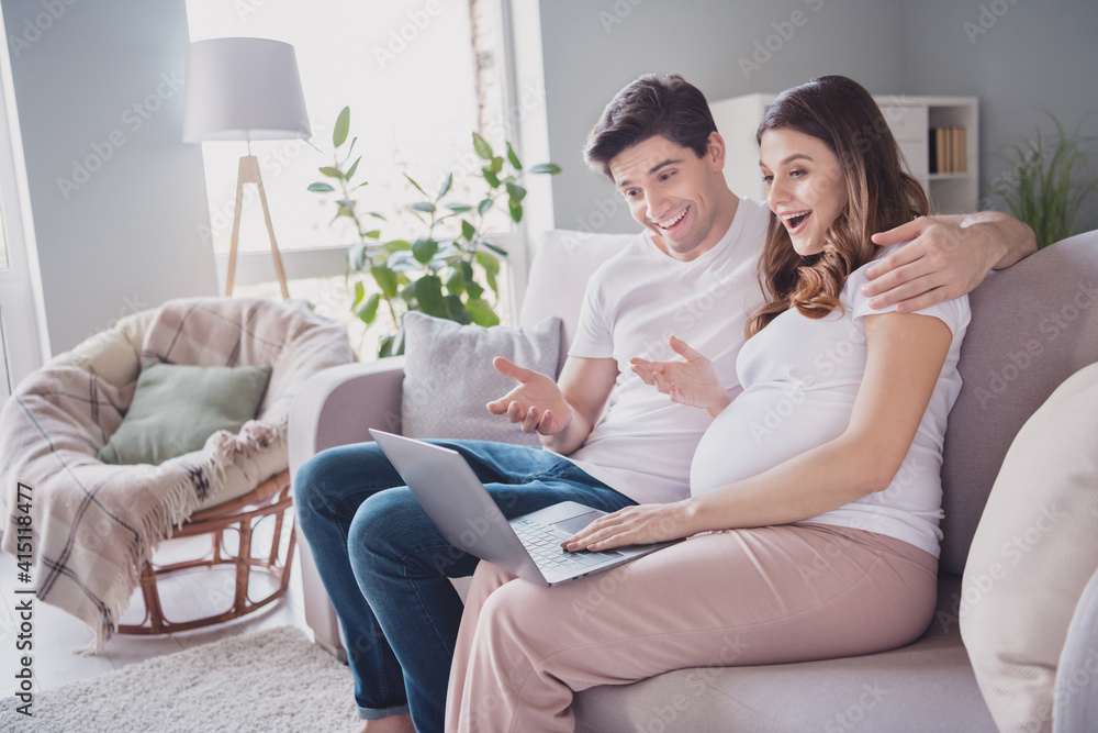 Profile side photo of positive adorable sweet pretty family waiting baby sitting sofa hugging tummy talking modern device indoors inside Profile side photo of positive adorable sweet pretty family waiting baby sitting sofa hugging tummy talking modern device indoors inside