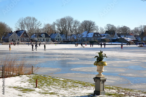 Photography Winter snow and people ice skating on frozen water in Broek in Waterland, a small town with traditional old and painted wooden houses, North Holland, Netherlands