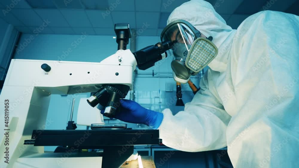 A man in a hazmat suit is operating a microscope in a laboratory A man in a hazmat suit is operating a microscope in a laboratory