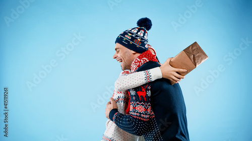 Woman with present hugging boyfriend in sweater on blue background