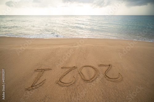 Handwriting year 2021 on sand and foam wave on beach.