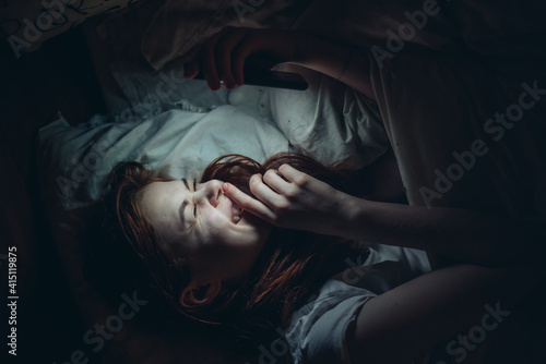 emotional woman with a phone in her hands lies in bed at night addiction © SHOTPRIME STUDIO