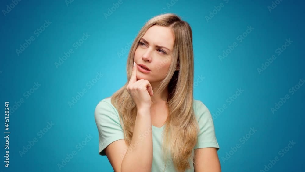 Thoughtful woman looking aside with pensive expression againast blue background Thoughtful woman looking aside with pensive expression againast blue background