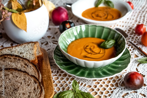 Tomato soup with freshly baked bread in vintage dishes on a fabric background